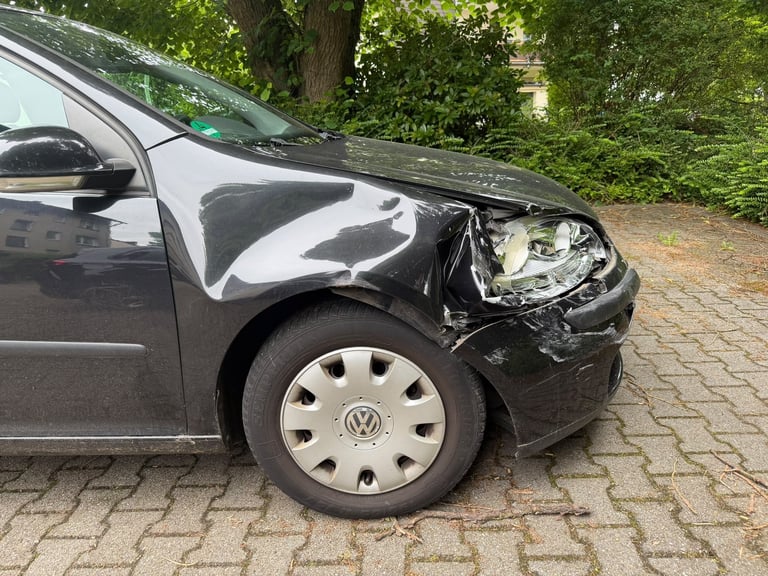 Eingedrückter vorderer Kotflügel und beschädigter Scheinwerfer an einem dunklen VW nach einem Zusammenstoß