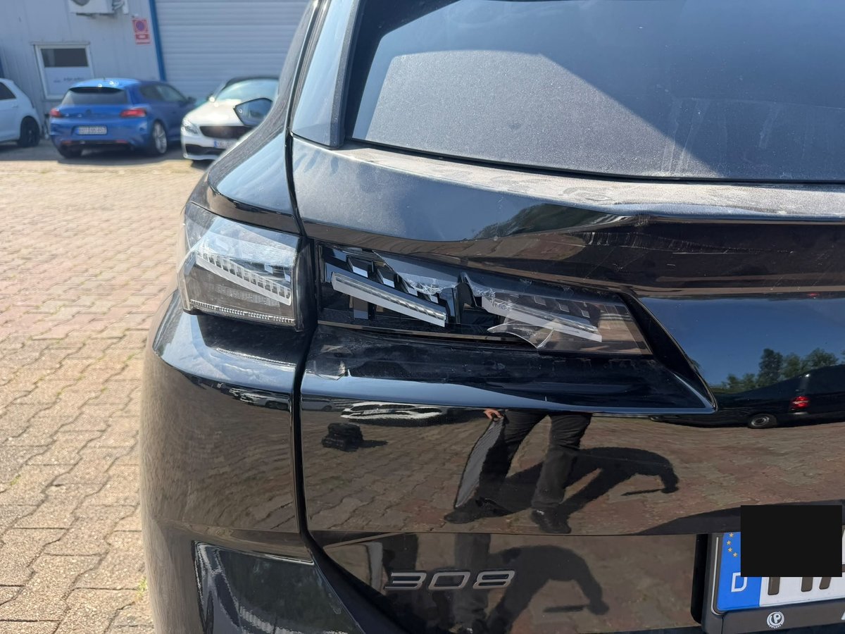 Beschädigte Rückleuchte und Heckklappenkante an einem schwarzen Peugeot 308 bei der Schadensaufnahme