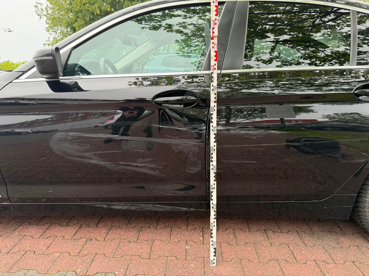 Dunkler BMW 5er im Profil mit angelegtem Messstab zur Ermittlung der Schadenshöhe